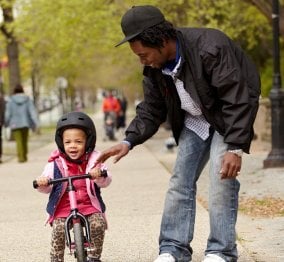 A father helping his young child ride a balance bike.