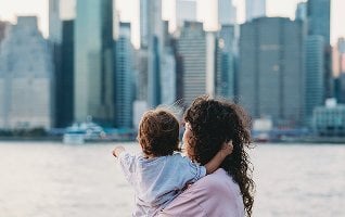 A woman holding a child, looking out at the Manhattan skyline.
